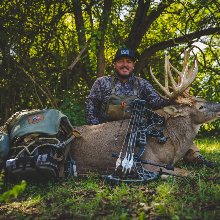 Man with a BullPath praxis saddle next to a large deer in a forest setting
